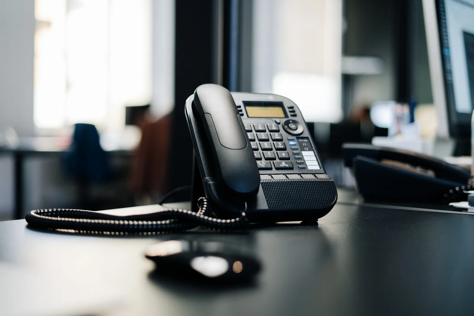 Black office desk phone with handset resting on a dark wooden table