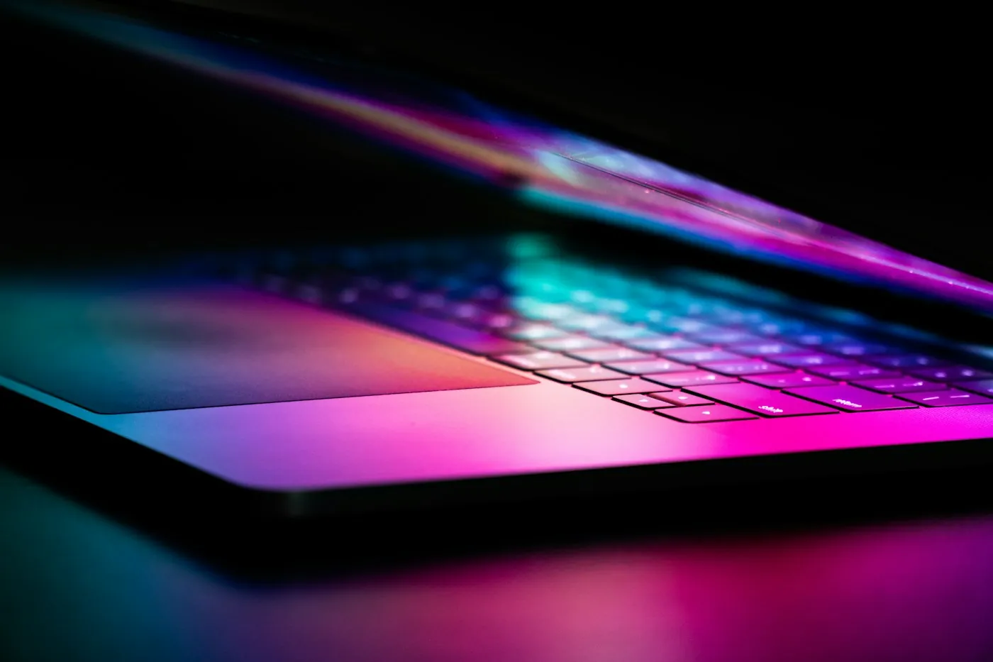 Laptop screen lit in violet and pink gradients on a dark desk